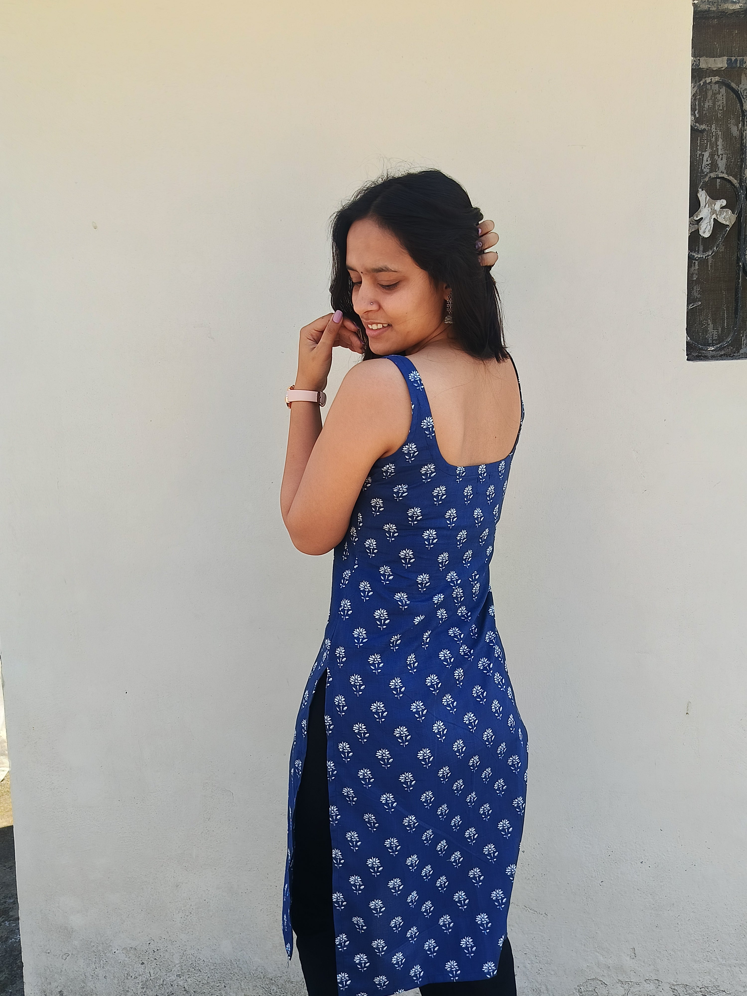 Woman wearing a blue patterned dress against a white wall.