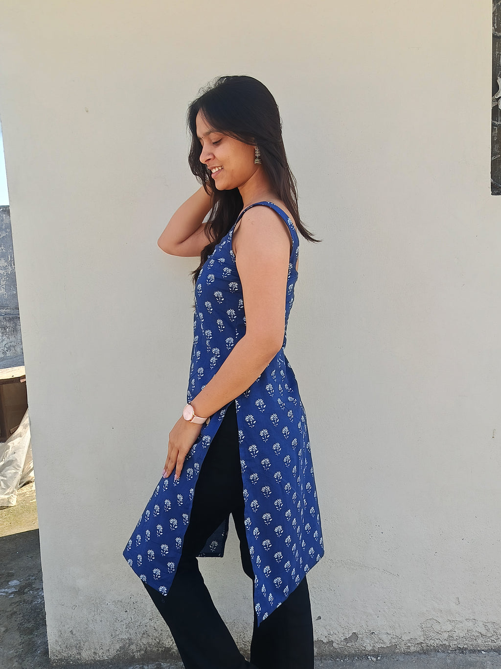 Woman wearing a blue patterned sleeveless top against a white wall.