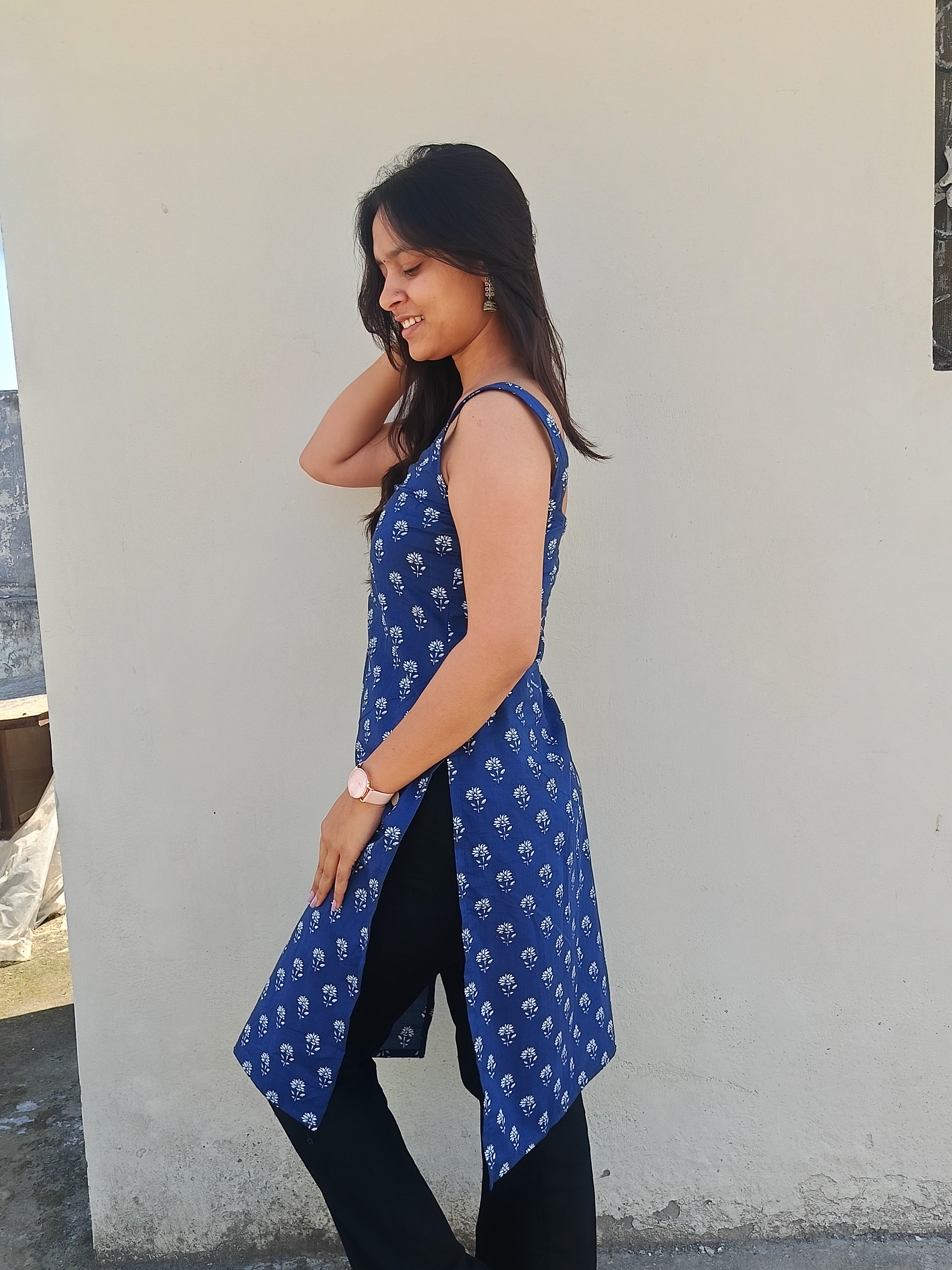 Woman wearing a blue patterned sleeveless top against a white wall.