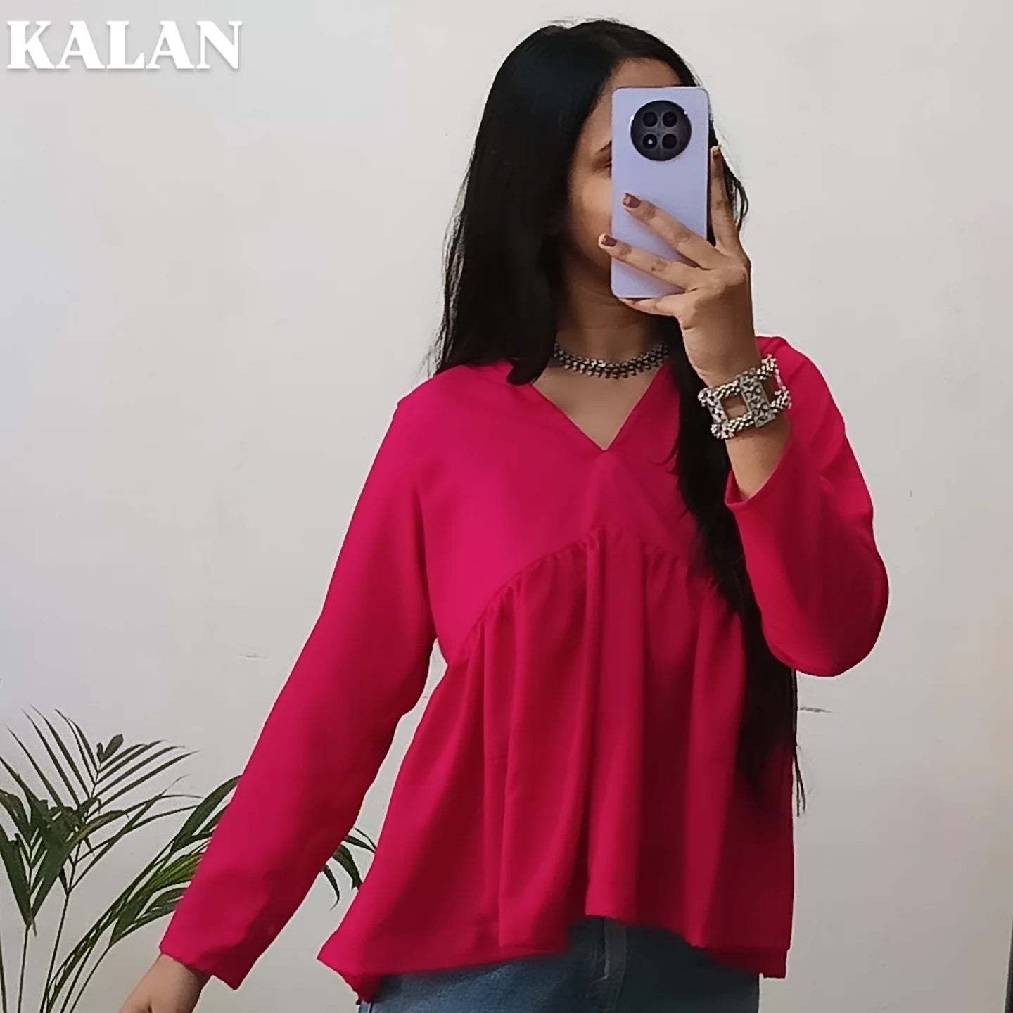 A woman wearing a pink peplum top with full sleeves, taking a mirror selfie with her phone.