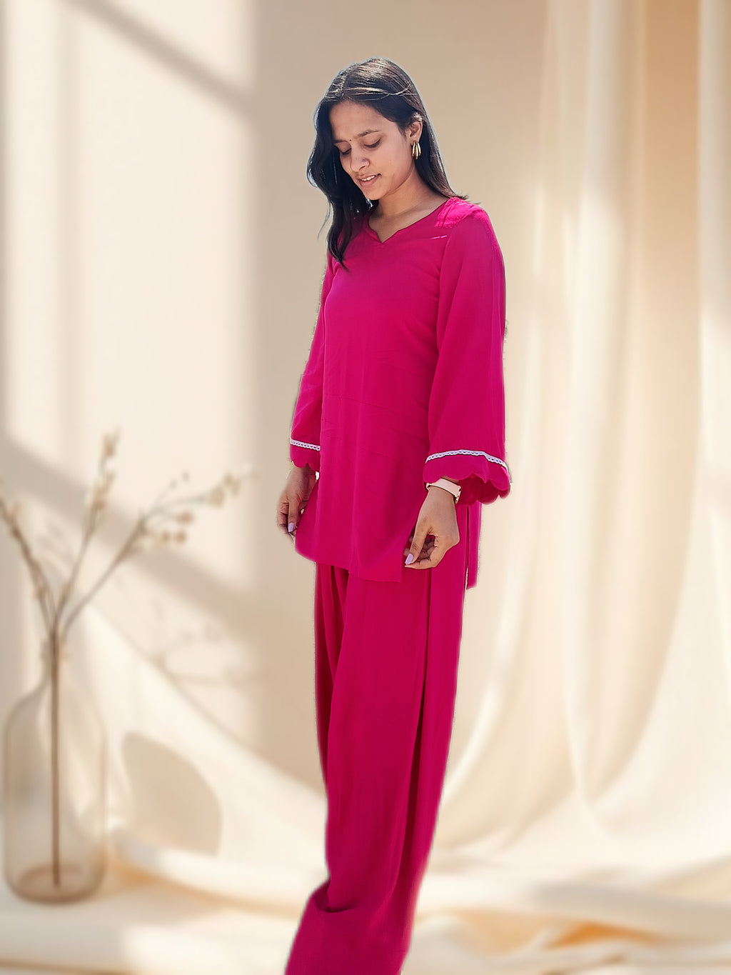 Woman wearing a bright pink salwar set in a softly lit room.