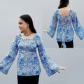 Woman wearing a blue patterned short kurti with a decorative back design, standing in front of a blue mosaic wall.