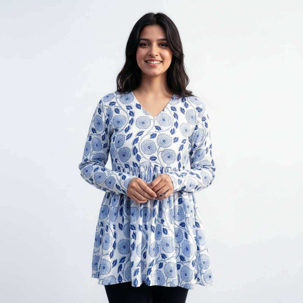 Woman wearing a blue floral kurti standing in front of a textured wall with floral patterns.