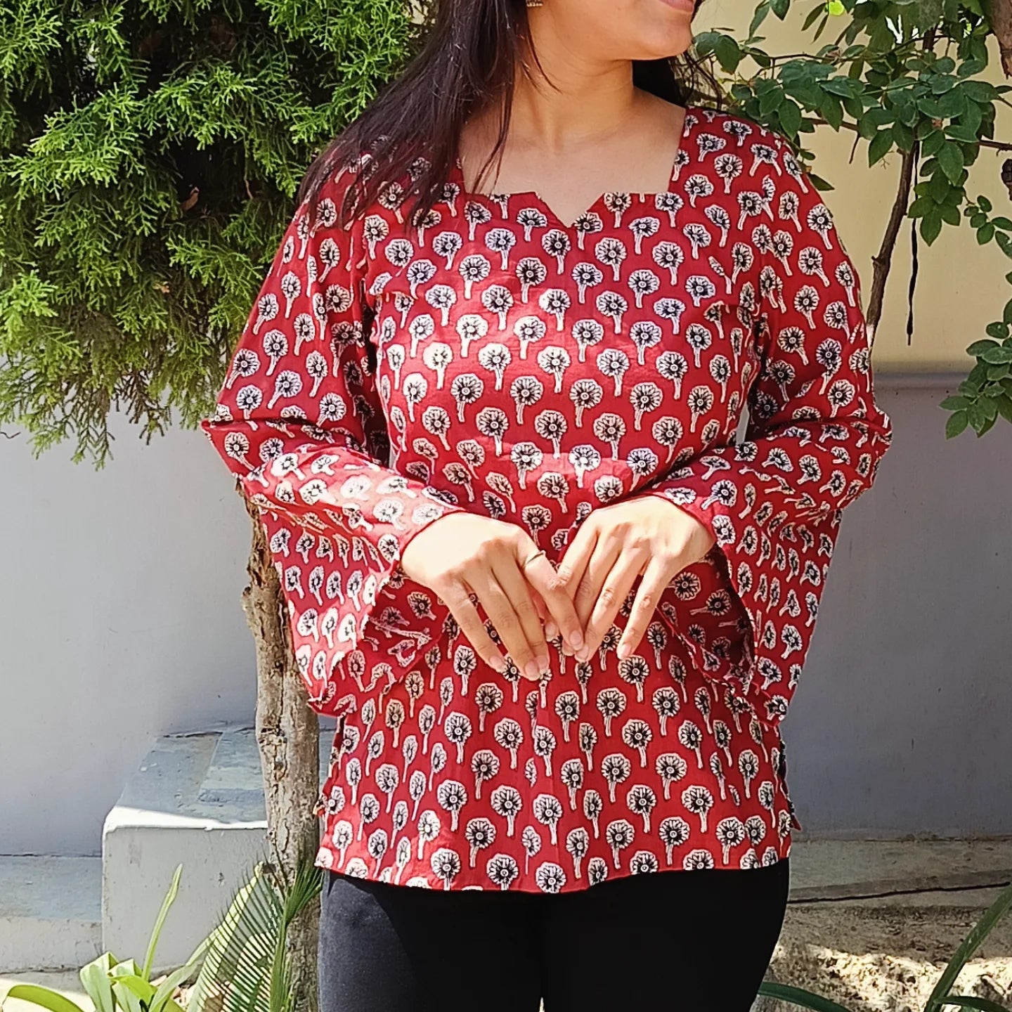 Person wearing a red patterned kurti  with greenery in the background