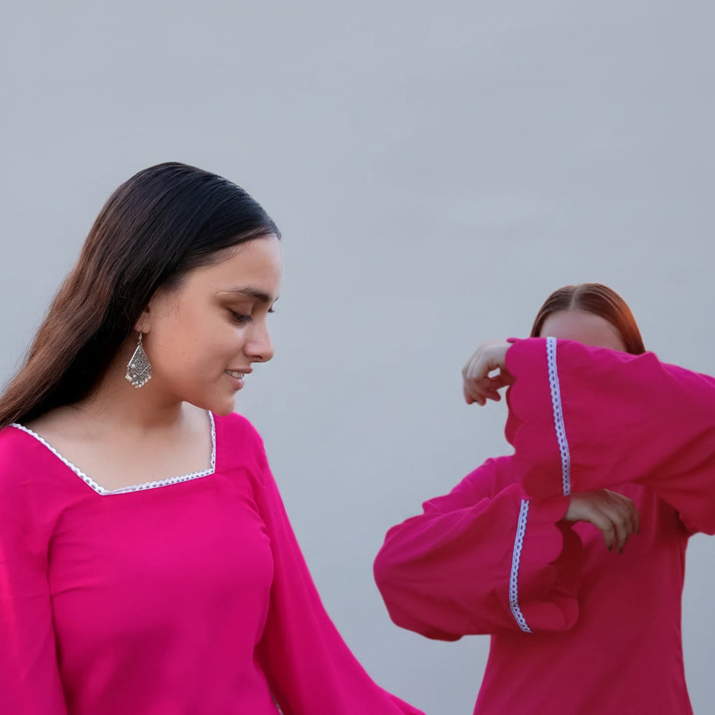 Two women in pink traditional outfits standing outdoors with floral decorations.
