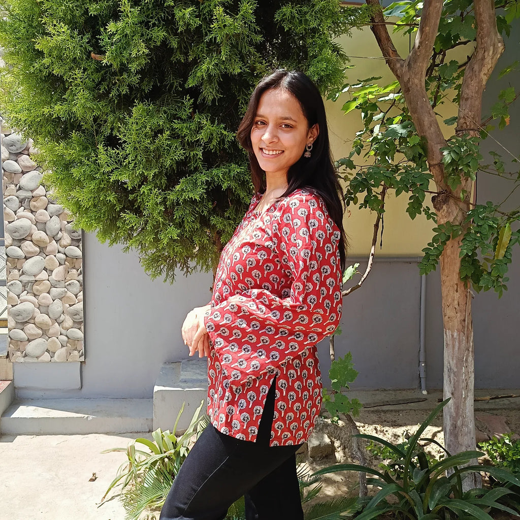 Woman in a red floral kurti standing outdoors with greenery around