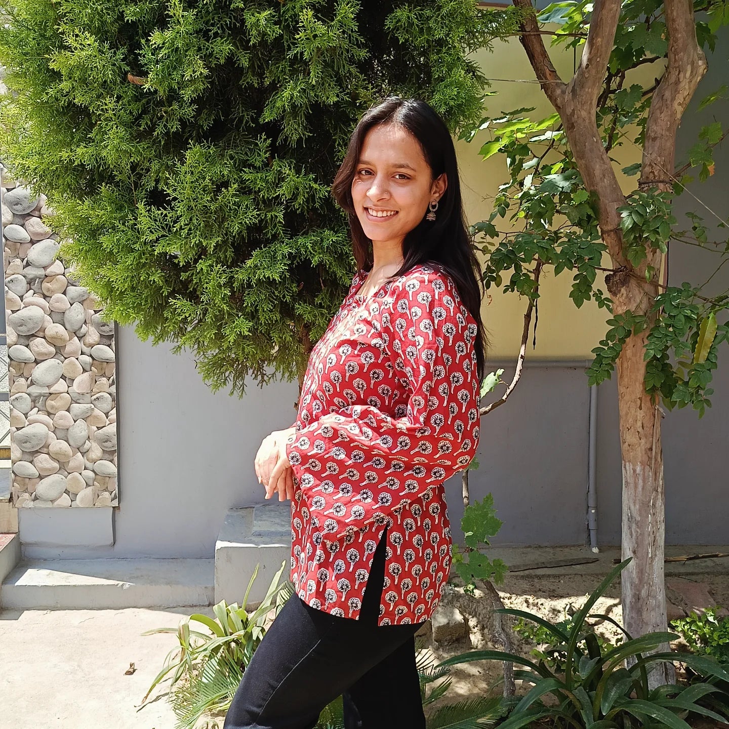 Woman in a red floral kurti standing outdoors with greenery around