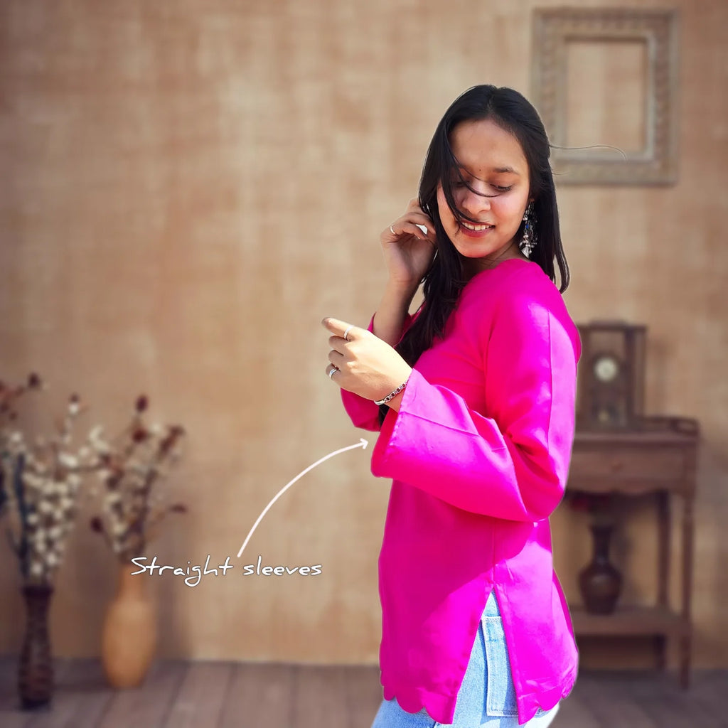 Woman wearing a bright pink top with straight sleeves in a room with a wooden floor and wall.