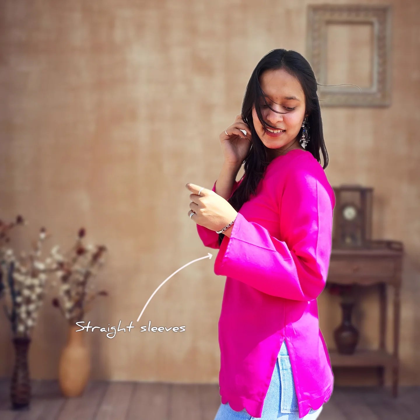 Woman wearing a bright pink top with straight sleeves in a room with a wooden floor and wall.