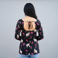 Woman wearing a black floral short kurti with open back, standing against a plain wall.