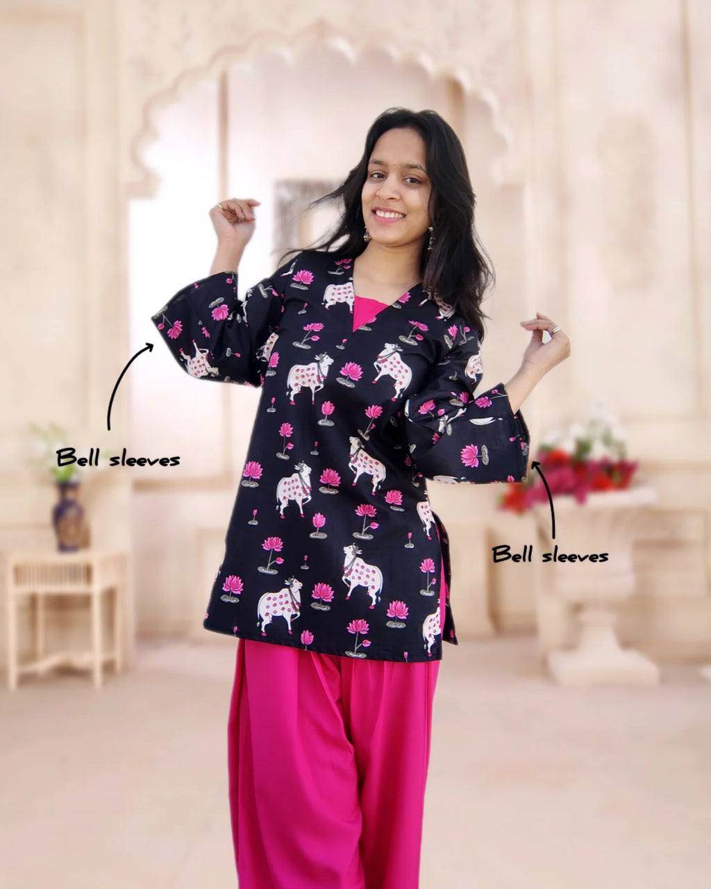 Woman wearing a black patterned top with pink farsi salwar in an indoor setting