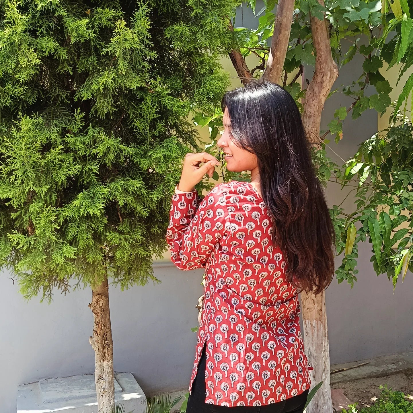 Woman in a red patterned kurti
standing outdoors with greenery around